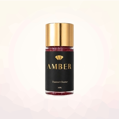 Amber Lash 30 mL tweezer cleaner bottle with a gold cap on a pale geometric background.

