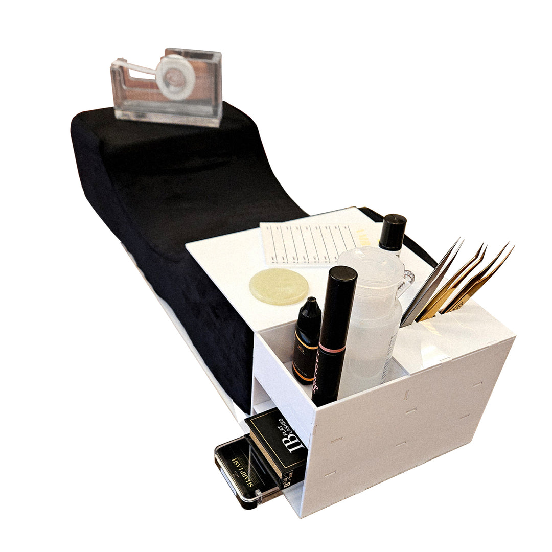 Close-up of white acrylic lash bed organizer with storage shelves and tool holders, loaded with tweezers, bottles, and lash accessories