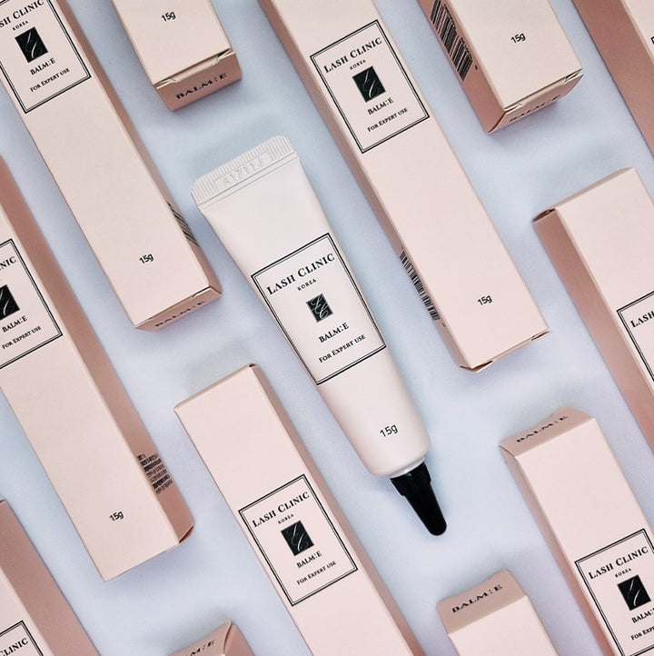Lash Clinic BALM:E 15 g conditioning balm tube surrounded by matching pink product boxes.